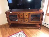 Front view of the wooden console table with glass-front doors, drawers, and bottom shelf, showing TV on top.