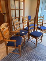 Group photo of six wooden dining chairs with blue upholstered seats, showing two captain chairs with armrests and four side chairs without armrests.