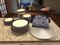Full view of dinnerware stacks with placemats and tablecloth on countertop