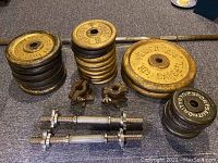 Photo showing stacks of yellow WEDER BARBELL weight plates with two star-shaped locking collars and two short arm curler bars in foreground.