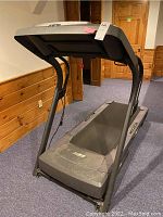 Side view of the treadmill showing the running belt, frame, and part of the room.