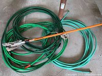 Photo of three coiled green garden hoses and an orange-handled tree pruner laid on garage floor
