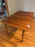 Photo of wooden rectangular kitchen table with one 20 inch leaf attached, showing turned legs and wood grain top surface in a warm brown finish.