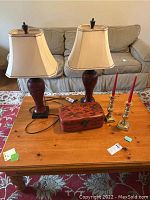 Wooden leaf motif lamps with cream-colored shades, brass candlestick holders with red candles, and vintage Asian lacquer box on wooden coffee table.