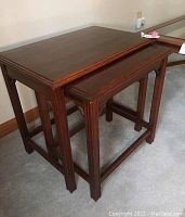 Two dark wooden nesting tables shown side by side with the smaller one partially nested under the larger.
