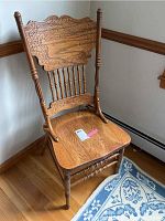 Oak wood dining chair with detailed carved backrest and spindled supports shown from front angled view.