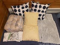 All pillows, cushions, rugs, and folded shower curtain with clips displayed together on a floor.