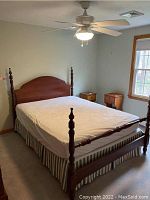 Full view of wooden queen size four post bed with white mattress cover and two matching nightstands near window