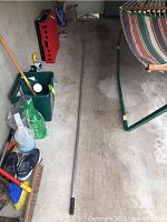 Full length photo of the metal roof rake pole laid out on a garage floor beside other miscellaneous items.