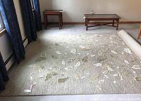 Full view of the Martha Stewart wool and viscose area rug on a floor with window curtains and wooden tables in the background, showing the stone gray base and vine leaf pattern.