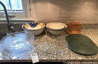 Frosted glass bowl, floral ceramic bowls, Crate & Barrel bowls, wooden napkin holder and green marble tray on kitchen counter.