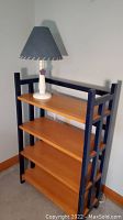 Front view of wooden shelf unit with table lamp placed on top, showing shelf shelves and lamp shade detail