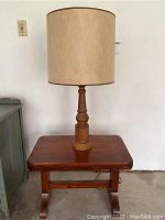 Side table with lamp and beige lampshade placed on top, showing full setup against wall.