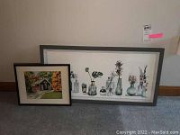 Two framed and matted watercolor paintings, one horizontal with bottles and plants, one smaller with a school building scene, both with signatures visible.