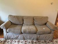 Front view of tan fabric sofa with three seat and back cushions and visible wear on cushions
