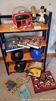 Shelf displaying a New England Patriots football helmet, three bobble head sports figures, three souvenir baseball caps, and assorted sports and humor books.