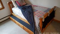 Pine wood twin size trundle bed with bedding, upper bed visible with pull-out trundle partially open below.