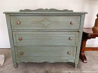 Front view of the vintage dresser showing all three drawers, carved detail on top drawer, the ornate metal handles, scalloped bottom edge and decorative back edge of top surface.