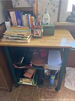 Front view of bar cart showing books stacked on top and lower shelves with various items including folded linens and household spray can.