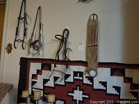 Photo showing vintage leather horse bridles and bit hanging above southwestern flat weave rug on wall with partial view of candles below.