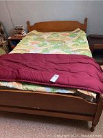 Front view of full size wooden bed with quilt and red throw showing headboard design