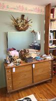 Full front view of the dresser with wall mirror above, showing the dresser surface with various small items and the flower decoration on the wall above the mirror.
