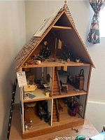 Front view of the three-story miniature Victorian house showing detailed interior with stairs and furniture on each floor.