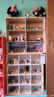 Overall view of two wooden shelves each with multiple compartments holding assorted miniature and figurine collectibles, including plush birds on top and various animal and Disney figures in compartments.