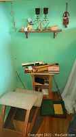 Wide photo showing padded stool, small wooden wall shelf with candle holders, figurines, musical instruments including vintage Echo harmonica in box, and more items on and below shelf.