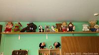 Wide view of several plush toys displayed on a high wooden shelf including various bears, cartoon characters, and animal plush dolls.