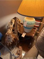Southwestern pottery lamp with light blue, cream, and tan geometric patterns, topped with pleated tan lampshade; hand-carved wood Native American sculpture with bear headdress; woven ladder with fur, feathers, and bead adornments.