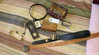 Various vintage belts, a wooden puzzle box, a box of marbles, small bag, pen, and accessories spread out on a blanket.