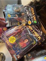 Photo showing various Star Trek Deep Space Nine figures in original blister packs, including Commander Benjamin Sisko figure with series branding and accessories.
