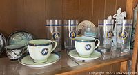 Set of 2 cups and saucers, and 4 tall glasses on a wooden shelf, each decorated with Star Trek Starship Enterprise logos
