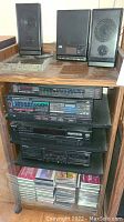 Stereo system components stacked on wood shelving including Sony and Pioneer branded equipment and small speakers with multiple CDs stored below.