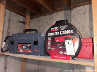 Photo of two toolboxes and EverStart booster cables on a wooden shelf in a basement with concrete walls.