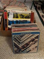 Cardboard box filled with multiple vinyl LP records, spines visible including The Police 'Synchronicity'