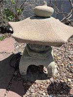 Photo of a tall cement pagoda statue with wide roof shaped like a spout and rounded finial top in a garden setting