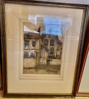 Framed art print showing rustic houses with brown wooden frame and layered mat