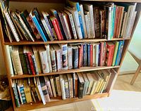 Three-shelf wooden bookcase filled with over 100 assorted books and magazines.