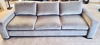 Mid-century style couch upholstered in light gray fabric with subtle vertical stripes, three seat cushions visible from front view.