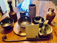 Group of pottery bowls, pitchers, decorative bottle, wooden tray, mallet, and juicer displayed on a table