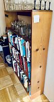 Side view of wooden shelf unit showing glassware on top shelf and books on lower shelves.