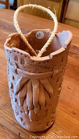 Photo of light brown ceramic vase with rope handle, textured front design, and handmade appearance