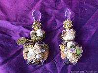 Front view of two ornate perfume bottles with floral decorations and crystal stoppers on purple fabric background