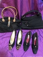 Two black leather purses and two pairs of distinctive retro style ladies shoes on purple fabric background.