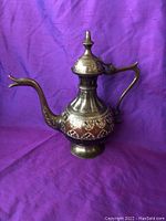 Antique Moroccan stamped brass tea pot showing a profile including stamped and enamel details, curved spout, and ornate handle.