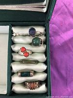 Photo of seven assorted rings arranged in a green cushioned ring box showing details of stone colors and settings.
