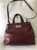 Front view of merlot Furla handbag with top handles and adjustable shoulder strap, showing leather surface and shape.