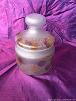 Ceramic honey pot showing abstract pastel hand painted designs on the lid and body, with a rounded knob lid.